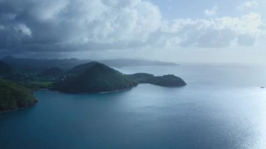İHA kamerası bulutlu bir günde tepenin etrafında yelken açan bir yatı çekiyor (Saint Lucia)