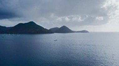 İnsansız hava aracı, sakin bir denizdeki yatları görüyor, kıyıda karanlık dağlar ve beyaz evler var (Rodney Bay, Saint Lucia)