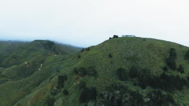 Kamera drona zbliża się do dużego domu na szczycie pasma górskiego we mgle Kalifornia, USA — Wideo stockowe