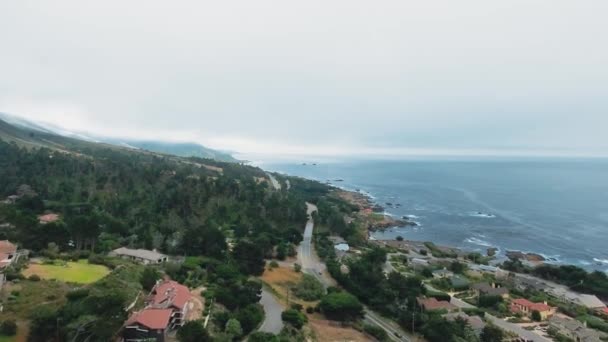 Drone disparando en un día de niebla. Océano, ciudad costera, casas, caminos, coches que pasan, bosque verde denso California, EE.UU. — Vídeo de stock