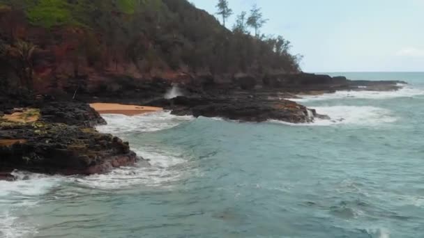 Drone kamera mozog víz felett fröccsenő egy sziklás parton Kauai, Hawaii, USA — Stock videók
