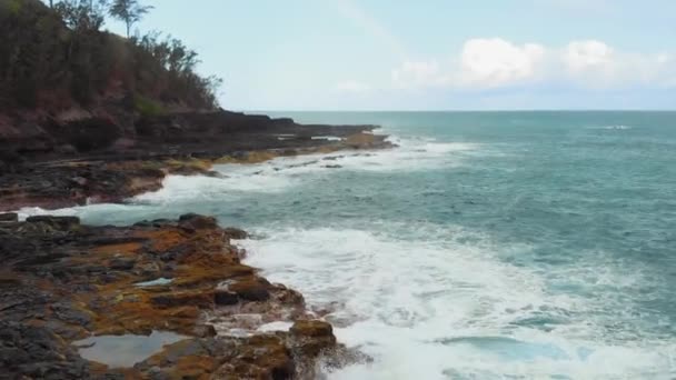Drone kamera mozog át a habzó hullámok ütő sziklás parton egy tiszta napon Kauai, Hawaii, USA — Stock videók