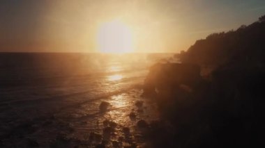 El Matador Sahili 'ndeki kayaların üzerinden yükselen insansız hava aracı kamerası Malibu, Califronia, ABD' deki parlak batan güneşe doğru yöneldi.