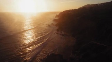 Okyanus yüzeyindeki güneşli yolun insansız hava aracı görüntüsü ve El Matador Beach, Malibu, Califronia, ABD 'deki karanlık kıyı.