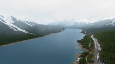 Kanada, Alberta 'da karlı zirveleri olan karanlık dağlar arasındaki Sprey Göller Barajı' nın görüntüsünü gösteren hava videosu