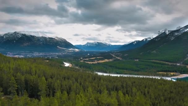 ドローンはカナダのアルバータ州の森林と町と雪の山の間の谷を撮影します — ストック動画