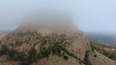 İnsansız hava aracı Wyoming, ABD 'deki Şeytani Kule kayalarının tepesine uçuyor. Tepesi bulutlarda saklanıyor.