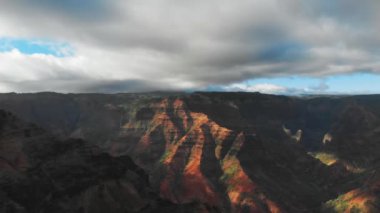 İHA kamerası bulutlu gökyüzünün altından kalkıyor Waimea Kanyonu, Kauai, Hawaii 'deki dağ sırasının zirvelerine dokunuyor.
