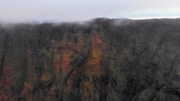 ドローンカメラは、ハワイ州カウアイ島ワイメア・キャニオンの雲の下で高い山脈を離陸します — ストック動画