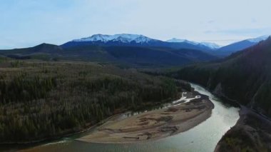 Dumanlı Nehir 'in yoğun bir ormandaki hava görüntüleri, ufuktaki dağ zirveleri (Alberta, Kanada)