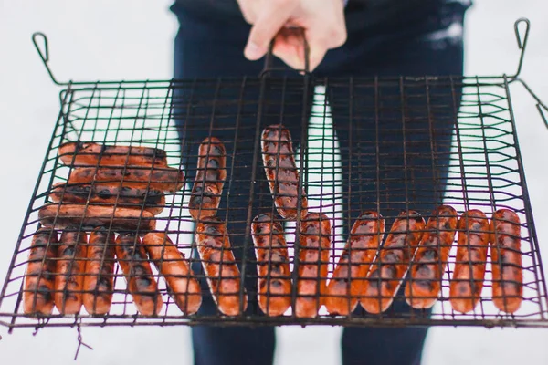 A man holding sausages fried on a fire