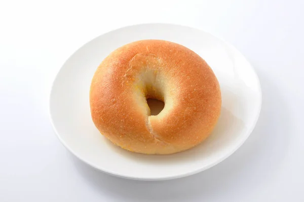Zwykły chleb Bagel na płycie na białym tle — Zdjęcie stockowe