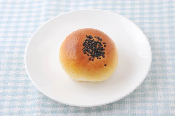Round bread with sesame on plate on table cloth — Stock Photo, Image