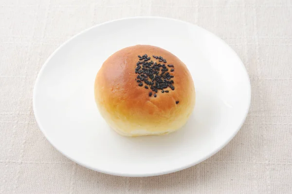 Round bread with sesame on plate on table cloth — Stock Photo, Image