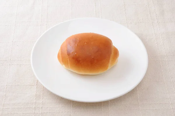 Butter bread roll on a plate on tablecloth — Stock Photo, Image