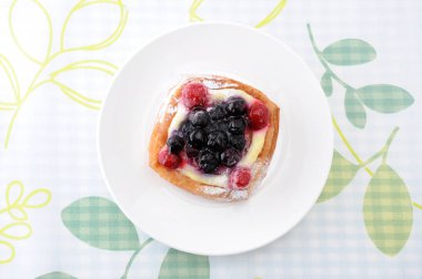 masa örtüsü üzerinde bir tabak üzerinde muhallebi krema ile yaban mersini kek