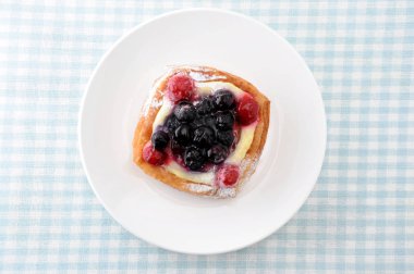 masa örtüsü üzerinde bir tabak üzerinde muhallebi krema ile yaban mersini kek