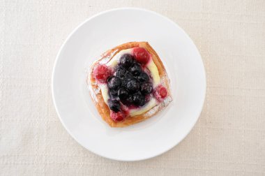 masa örtüsü üzerinde bir tabak üzerinde muhallebi krema ile yaban mersini kek