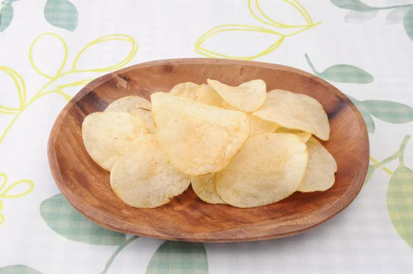 Картофельные чипсы на деревянной тарелке на скатерти — стоковое фото