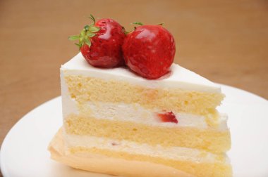 ahşap masada tabakta çilek sünger kek parçası