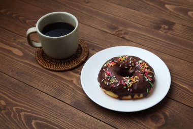 Tabakta çikolatalı donut ve ahşap masada sıcak kahve.