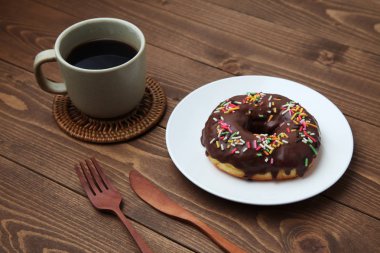 Tabakta çikolatalı donut ve ahşap masada sıcak kahve.
