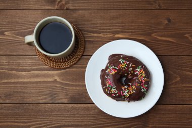 Tabakta çikolatalı donut ve ahşap masada sıcak kahve.