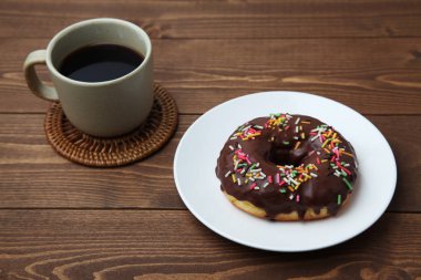 Tabakta çikolatalı donut ve ahşap masada sıcak kahve.