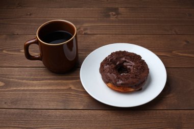 ahşap masada izole sıcak kahve ile tabakta çikolata buzlu çörek