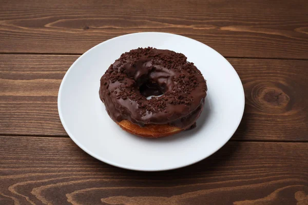 Chocolate frosted doughnut on plate isolated on wooden table — Stock Photo, Image