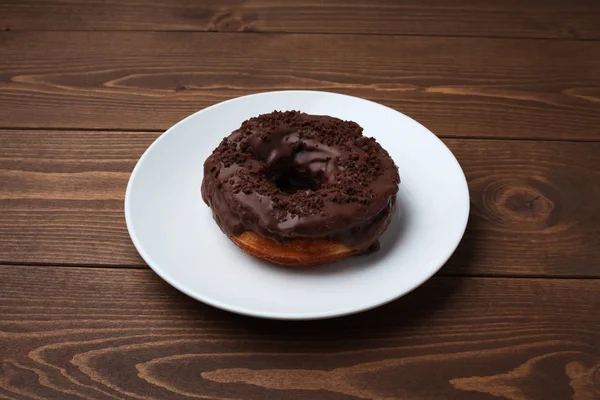 Chocolate frosted doughnut on plate isolated on wooden table — Stock Photo, Image
