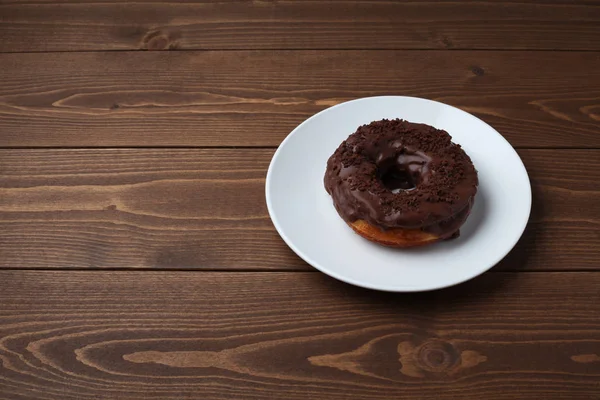 Chocolate frosted doughnut on plate isolated on wooden table — Stock Photo, Image