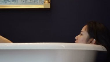 Asyalı kadın dinlenmek ve köpük video 4 k ile küvet içinde banyo