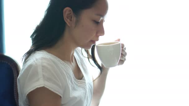 Mulher Asiática Sentado Janela Iluminada Beber Xícara Café Relaxar Feliz — Vídeo de Stock