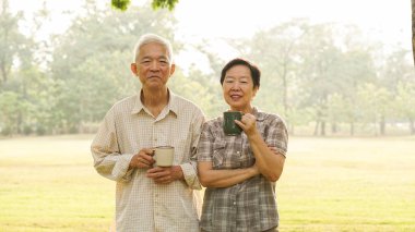 Asian elderly couple drink tea coffee in moring park clipart