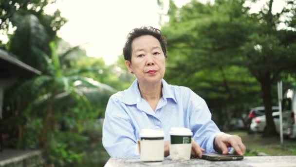 亚洲老年妇女独自在公园等咖啡 — 图库视频影像