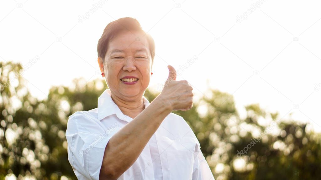 Happy Asian elderly woman smiling in morning sun with green nature background