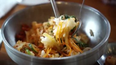 Bibimbap Korece pirinç ve paslanmaz kaşık kullanarak çeşitli sebze gıda kapları karıştırma