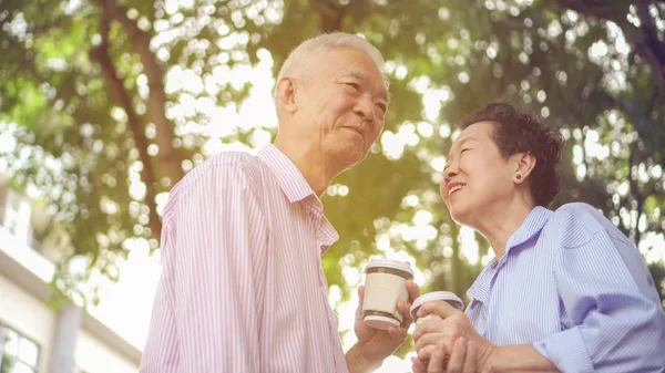 幸せなアジア高齢者カップル コーヒーを飲みながら緑豊かな街で朝散歩 — ストック写真