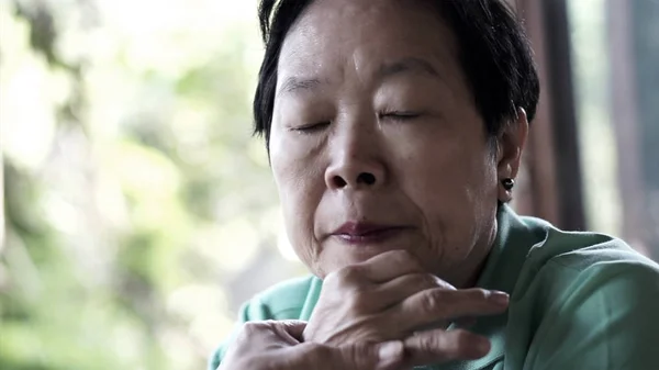 Азиатская старшая женщина с рукой на лице думает, беспокоиться грустно — стоковое фото