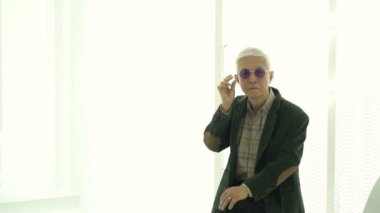 Asyalı yaşlı adam havalı bir takım elbise ve ağır çekimde güneş gözlüğü giyiyor.