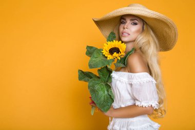 Ayçiçeği tutan bir beyaz elbise ve şapka giyen güzel bir kadın uzun sarı saçlı portresi.