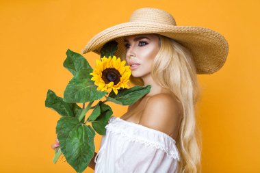 Ayçiçeği tutan bir beyaz elbise ve şapka giyen güzel bir kadın uzun sarı saçlı portresi.
