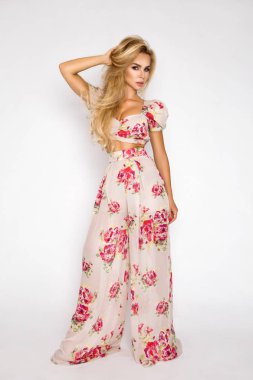 Sarı saçlı, seksi güzel, zarif kadın çiçek ve bir şapka ile şık giysileriyle stüdyosunda poz veriyor.