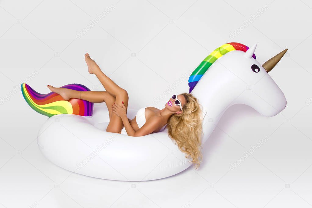 Beautiful, sexy blonde model in a elegant bikini, lies on a white unicorn. Hit the summer