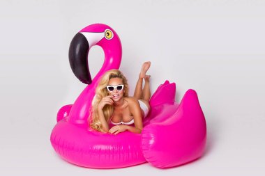 Zarif bir bikini, güzel, seksi sarışın model pembe flamingo üzerinde yatıyor. Yaz vurmak