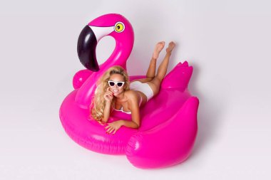 Zarif bir bikini, güzel, seksi sarışın model pembe flamingo üzerinde yatıyor. Yaz vurmak
