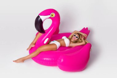 Zarif bir bikini, güzel, seksi sarışın model pembe flamingo üzerinde yatıyor. Yaz vurmak