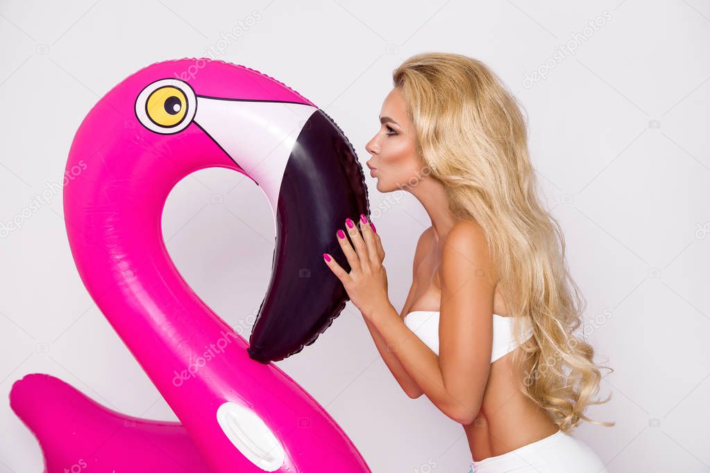Beautiful sexy blonde model in a elegant bikini with a pink flamingo. Hit the summer