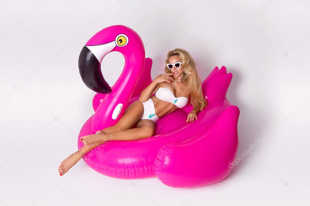 Beautiful, sexy blonde model in a elegant bikini, lies on a pink flamingo. Hit the summer